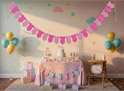 A baby shower party setup featuring a pink baby boot banner garland hanging across a wall, a decorated table with a tiered cake, pastel balloons, gift boxes, and a high chair in a decorated room.